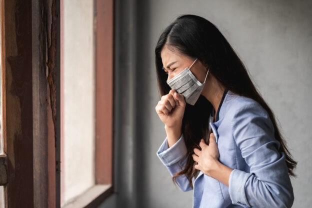 Mulher usando máscara protetora tossindo e sentindo desconforto no peito devido a alergias respiratórias