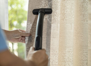 Pessoa realizando a limpeza de cortinas com mofo usando aspirador de pó próximo à janela.