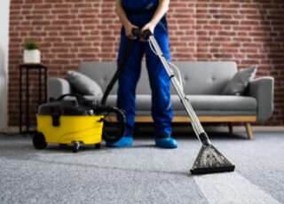 Profissional realizando limpeza de tapete com manchas utilizando equipamento a vapor em ambiente residencial.