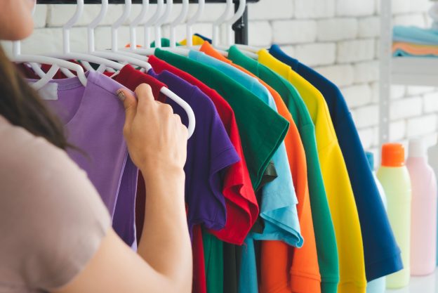 Roupas coloridas penduradas em cabides, organizadas por cor, representando cuidados profissionais para manter cores das roupas vivas por mais tempo.